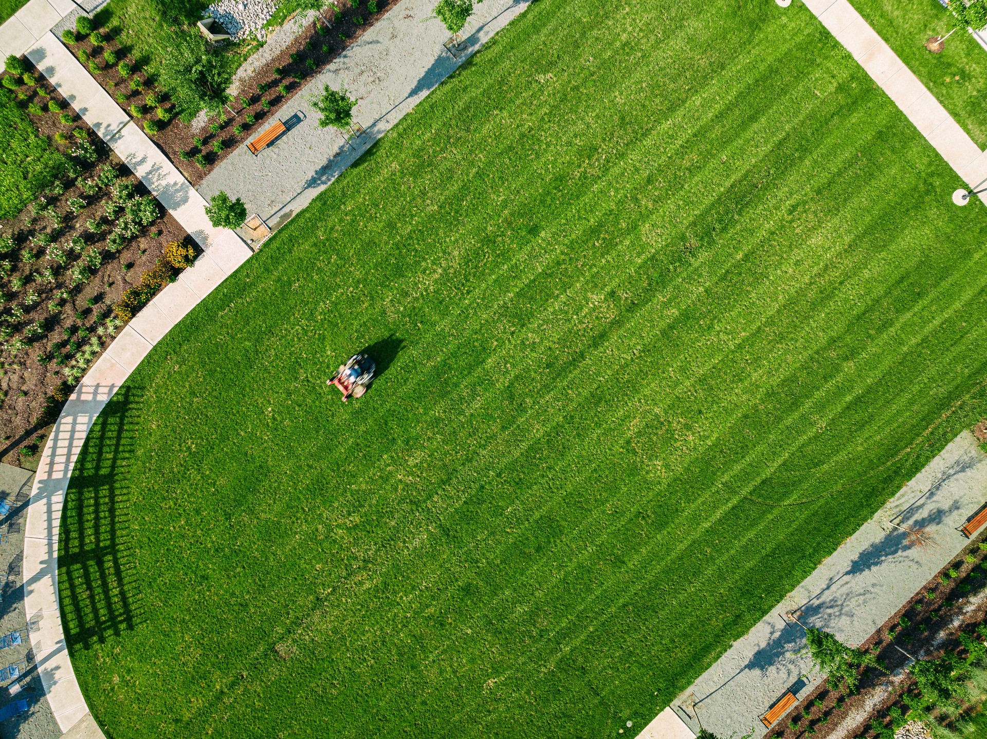 Elevated View of a Man Using a Riding Lawnmower to Cut Grass in Straight Lines